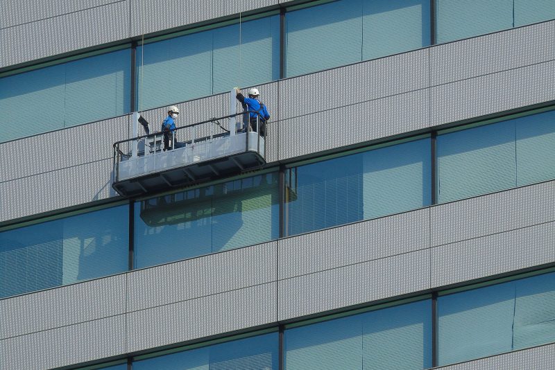 Due operatori puliscono le vetrate di una facciata continua da un cestello