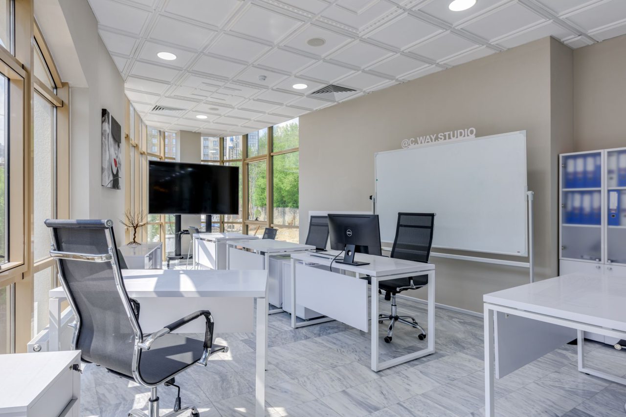Ufficio open space con scrivanie, grandi finestre e pavimento chiaro