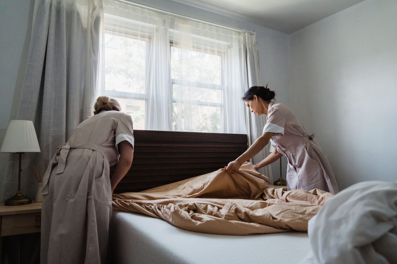 Due addette al piano rifanno il letto in una camera illuminata da luce naturale