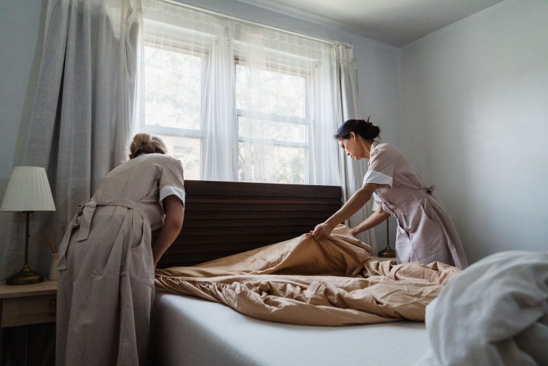 Due addette al piano rifanno il letto in una camera illuminata da luce naturale